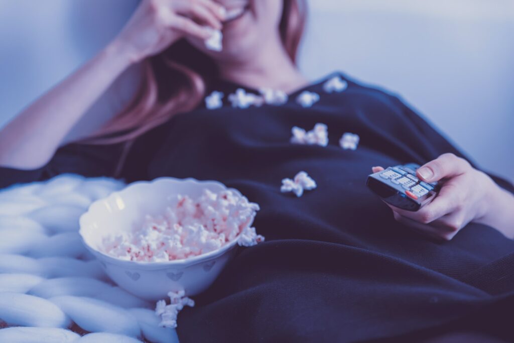 woman lying on bed while eating puff corn