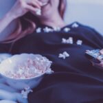 woman lying on bed while eating puff corn